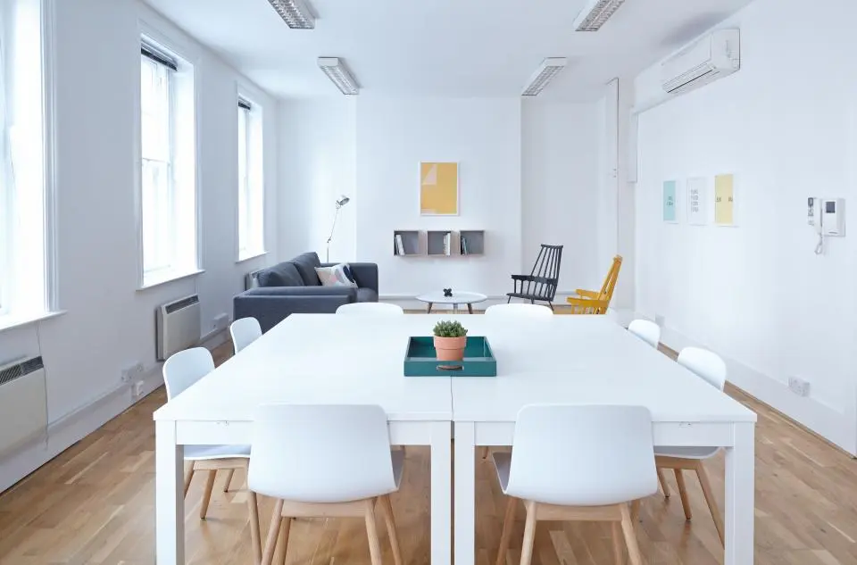 Open space de bureaux lumineux avec une grande table blanche, des chaises et un parquet propre