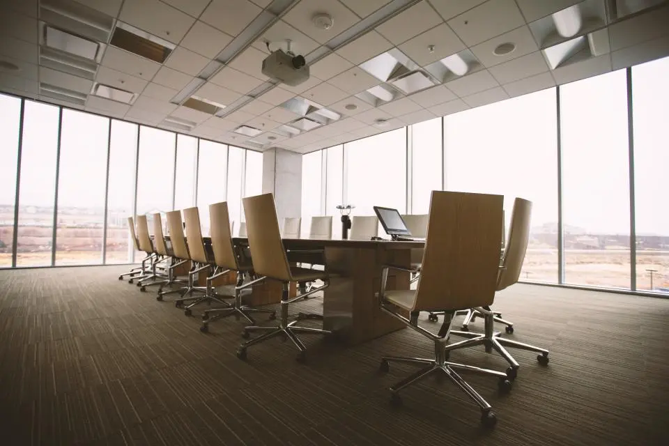 Salle de réunion vitrée avec une longue table et des fauteuils sur un parquet entretenu