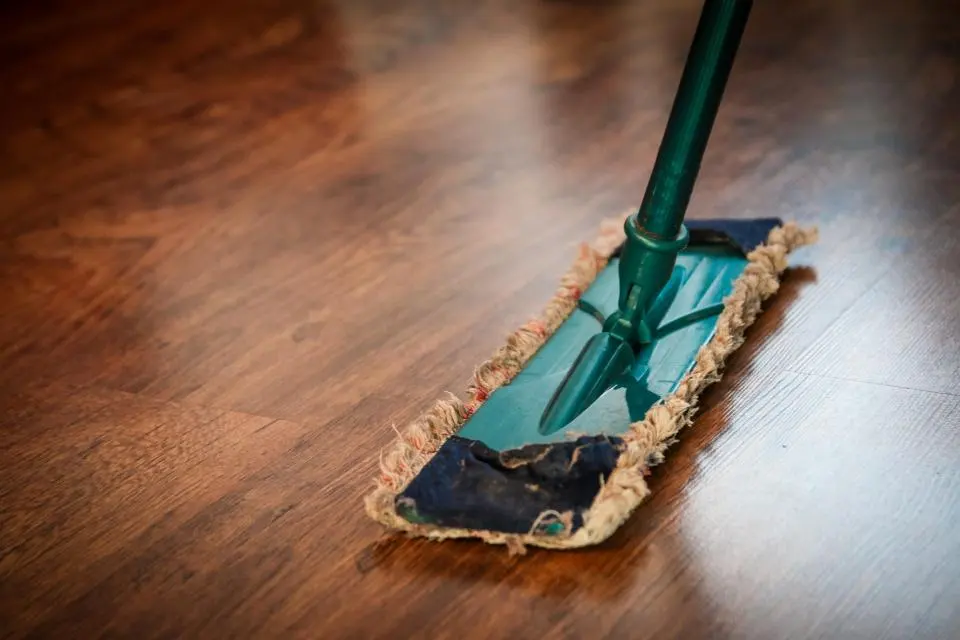 Balai à franges de nettoyage passé sur un parquet en bois